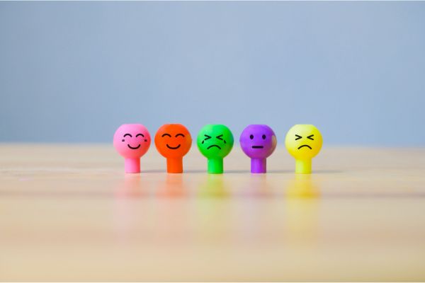 Emotional palette artwork with five colored, neck-and-head-shaped figures on a beige background, displaying diverse emotions like joy, sorrow, neutrality, and rage, representing the spectrum of human feelings for emotional intelligence.