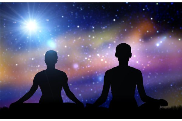 Two silhouettes of people meditating in cross-legged position on dark ground, against a vibrant cosmic background with stars, nebulae in shades of blue, purple, and orange, evoking inner peace and universal connection in mindfulness meditation.